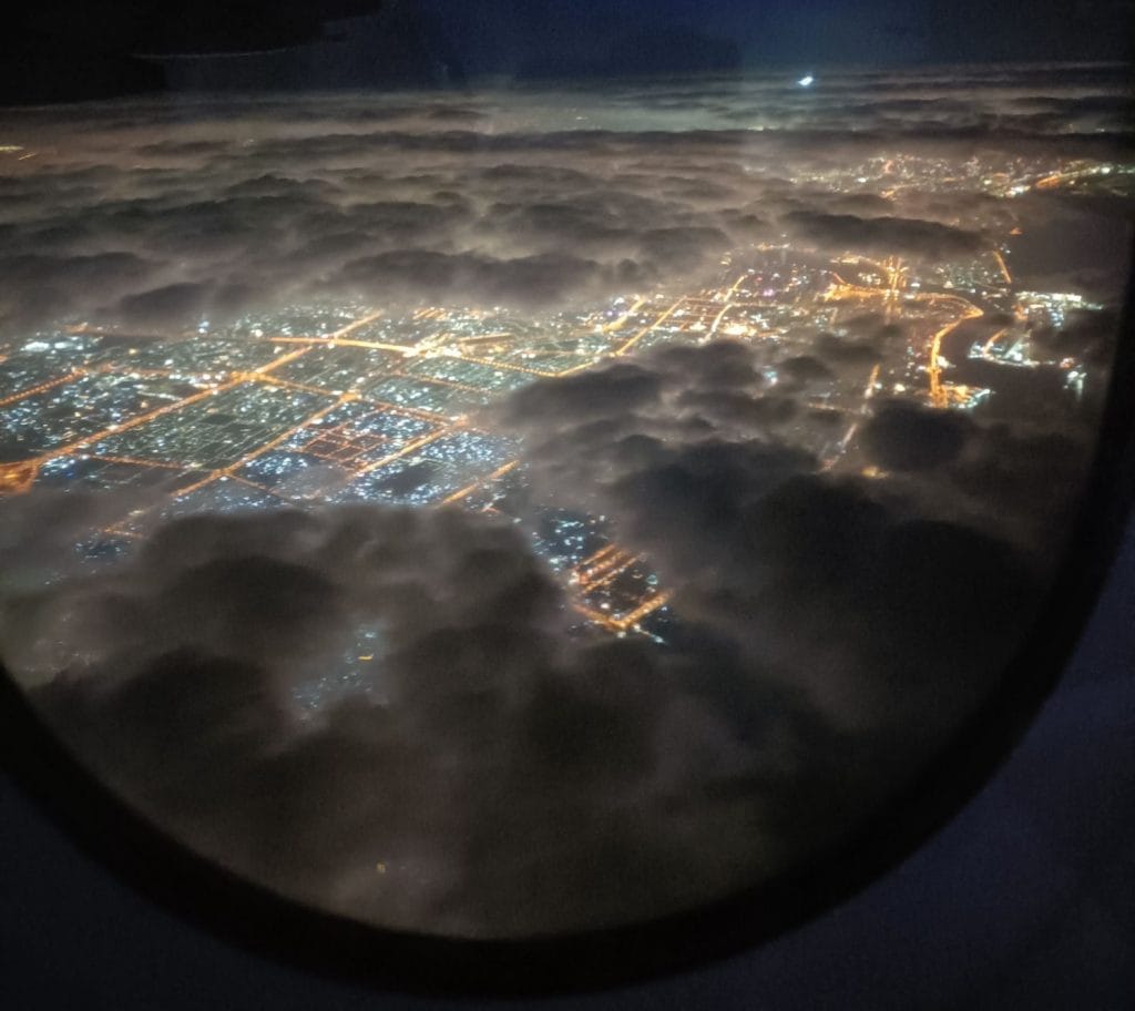view of dark clouds and bright citylights over Bangkok at night time from airplane window