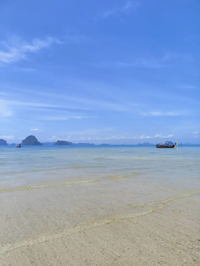 white sand beach with clear water in Thailand with a blue sky background and karsts