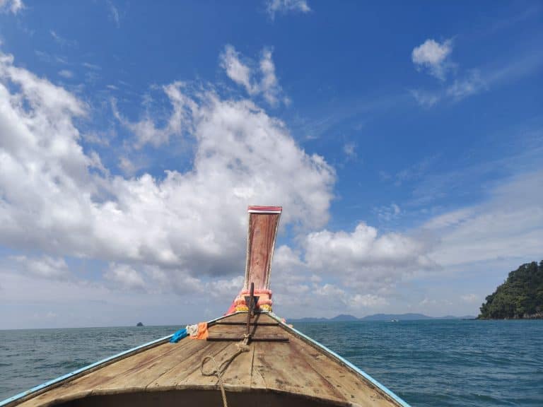 long tail boat with colourful buddhist scarves and blue sky behind with some white fluffy clouds and turquoise sea in Krabi
