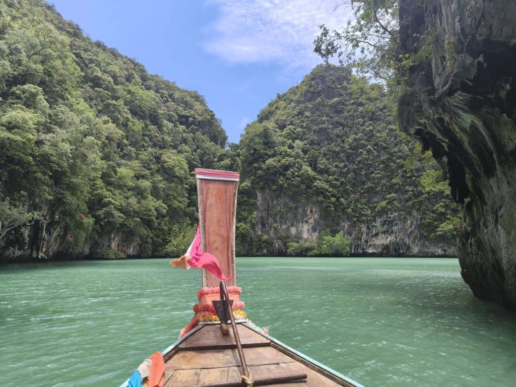 colourful material scarves on a wooden long tail boat in thailand floating on a turquoise sea and limestone, tree covered karsts in the background of the lagoon