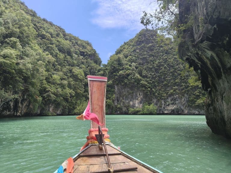 colourful material scarves on a wooden long tail boat in thailand floating on a turquoise sea and limestone, tree covered karsts in the background of the lagoon