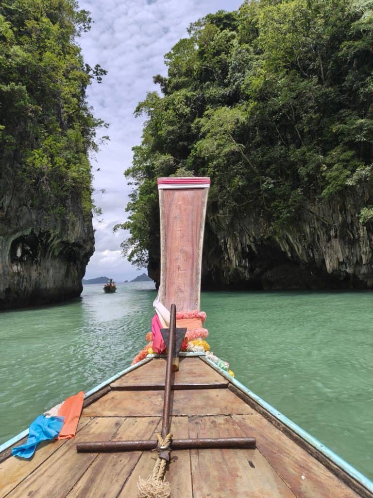 long tail boat in Thailand with colourful scarves on turquoise water and limestone karsts in a lagoon