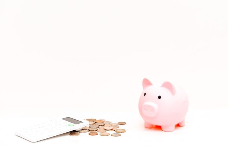 pink piggy bank next to some coins and a calculator on a white background